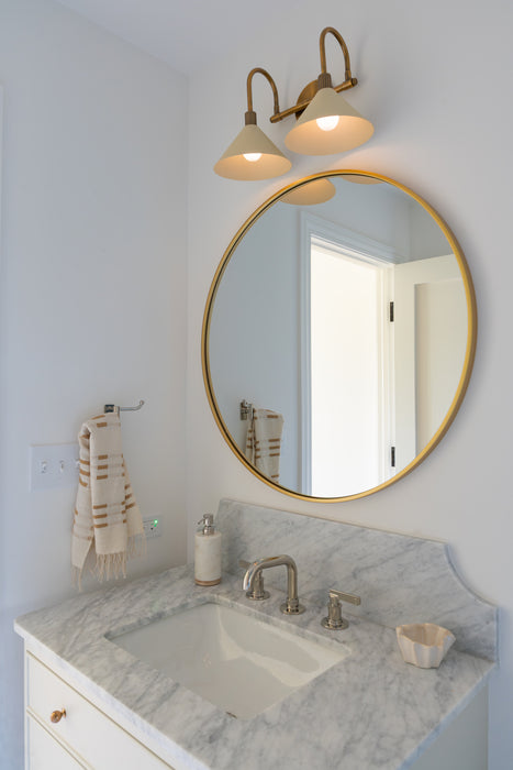 Bathroom vanity with round mirror, light fixture, and marble countertop.