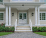 Front of a house with white columns, steps, and a gray driveway.