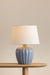 Table lamp with a ribbed ceramic base on a wooden table against a beige wall