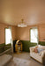 A nursery room with peach-colored walls, a green wainscoting panel, a white crib, a cream sofa with pillows, a floral rug, and a small yellow toy house organizer near the windows.