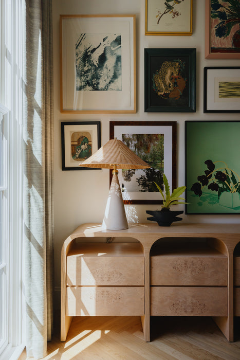 Wooden side table with lamp and decor against a wall with framed artwork