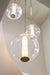 Close-up of three clear glass globe pendant lights with brass accents and glowing cylindrical light sources hanging from chains in a bright stairwell.