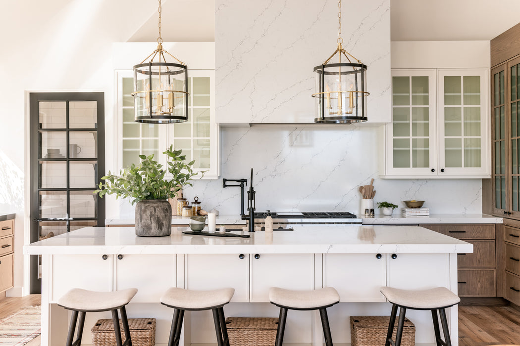 Bright kitchen with two lantern-style pendant lights hanging over a white island, marble backsplash, glass-front cabinets, and light wood cabinetry.