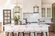 Bright kitchen with two lantern-style pendant lights hanging over a white island, marble backsplash, glass-front cabinets, and light wood cabinetry.