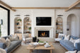 Bright living room with a modern fireplace and mounted TV, flanked by arched built-in shelves, wood ceiling beams, and blue upholstered sofas with neutral accent pillows.