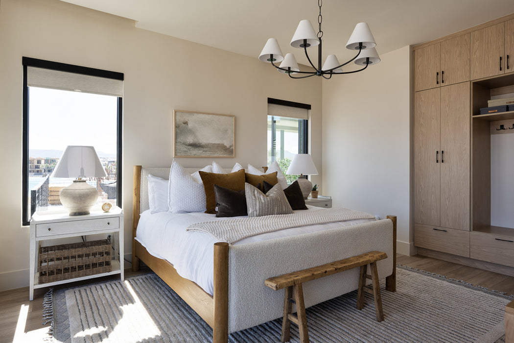 Bright, modern bedroom with a black chandelier featuring white shades centered above a wood bed with layered neutral bedding, nightstands with table lamps, and built-in wood cabinetry.