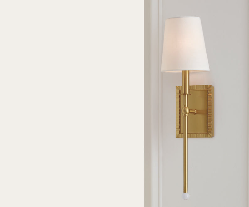 A brass wall light with a white light shade.