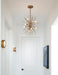 Modern gold chandelier in a hallway with white walls and a door.