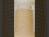 Wall-mounted sconce crafted from natural materials with layered, handcrafted detail. A curved raw silk shade forms a tunnel-like shape that shields and softens the light, while an outer layer of basket-woven cane wicker adds texture and depth. The light glows warmly through the layers, highlighting the contrast between the smooth silk and the woven exterior.