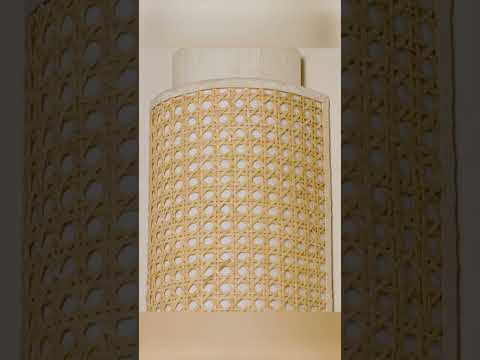 Wall-mounted sconce crafted from natural materials with layered, handcrafted detail. A curved raw silk shade forms a tunnel-like shape that shields and softens the light, while an outer layer of basket-woven cane wicker adds texture and depth. The light glows warmly through the layers, highlighting the contrast between the smooth silk and the woven exterior.