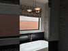 Modern bathroom with stone wall, white tub, black tile, and three light modern chandelier hanging above tub