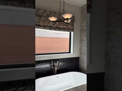 Modern bathroom with stone wall, white tub, black tile, and three light modern chandelier hanging above tub