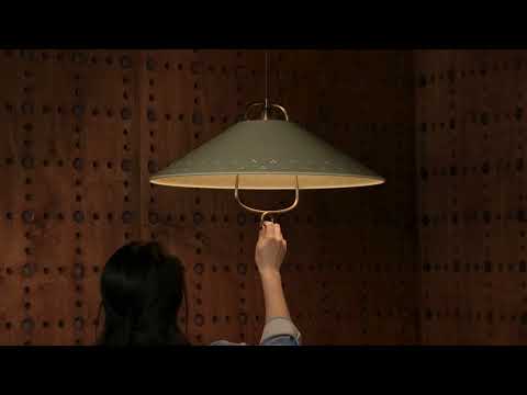 The pendant features a Soft Sand-colored shade with a smooth, muted tone, accented by a small decorative loop beneath it. Perforated detailing in the metal adds subtle texture and visual interest, allowing light to pass through in a soft pattern. The pendant is adjustable, allowing the height to be changed.
