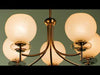Chandelier-style light fixture suspended from the ceiling, featuring multiple arms extending outward with evenly spaced light sources. The fixture emits a warm, ambient glow that illuminates the surrounding space. Its design combines clean lines with a balanced, symmetrical structure, serving as a central focal point while casting soft, even light throughout the room.