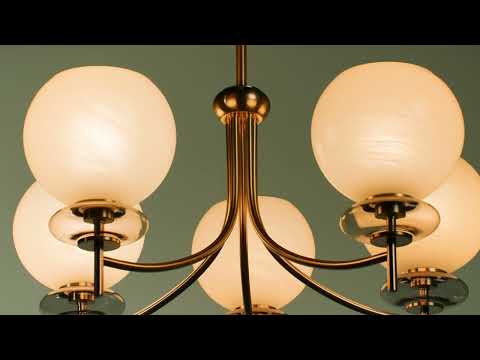 Chandelier-style light fixture suspended from the ceiling, featuring multiple arms extending outward with evenly spaced light sources. The fixture emits a warm, ambient glow that illuminates the surrounding space. Its design combines clean lines with a balanced, symmetrical structure, serving as a central focal point while casting soft, even light throughout the room.