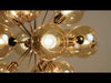 Chandelier-style light fixture suspended from the ceiling, featuring multiple amber glass shades. The warm-toned glass deepens the color of the light, creating a rich, golden glow. The fixture’s arrangement provides even illumination while the amber glass adds warmth and a soft, inviting ambiance to the space.