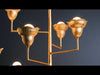 Vertical video of a chandelier-style light fixture hanging from the ceiling, featuring multiple arms and evenly spaced bulbs. The fixture emits a warm, diffused glow, creating soft, ambient lighting. Its structured, symmetrical design and floral details make it a central visual focal point while gently illuminating the surrounding space.