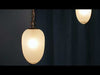 Swagged chandelier composed of multiple hanging pendants connected along draped cord chains to form a single fixture. Each pendant features milky, opaque glass shades that diffuse light into a soft, even glow. The suspended arrangement creates a flowing, layered effect, with light distributed across the space in a warm, ambient pattern.
